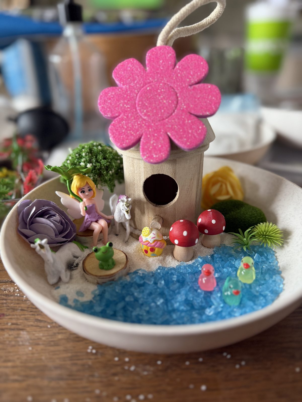 A finished fairy garden with a birdhouse, moss and a blue sand pond