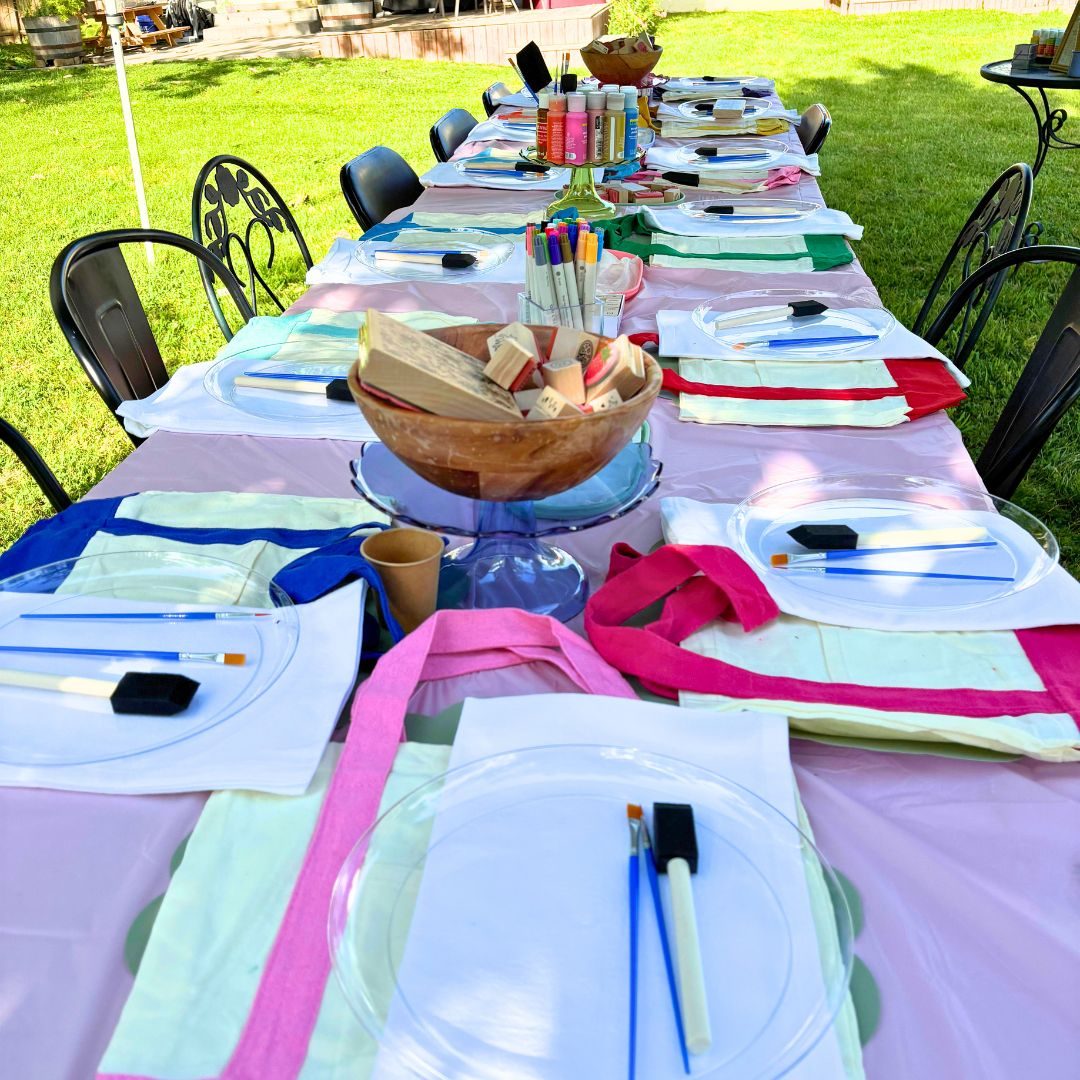 An outdoor party table set with paint plates, brushes and individual place settings