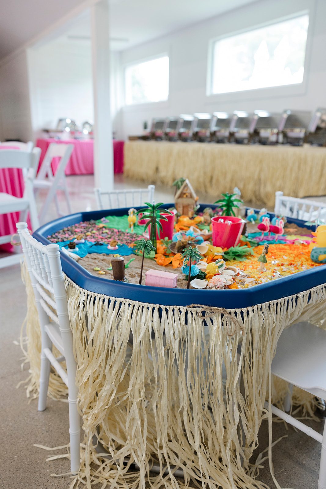 A sand and water sensory table styled with palms and a raffia skirt