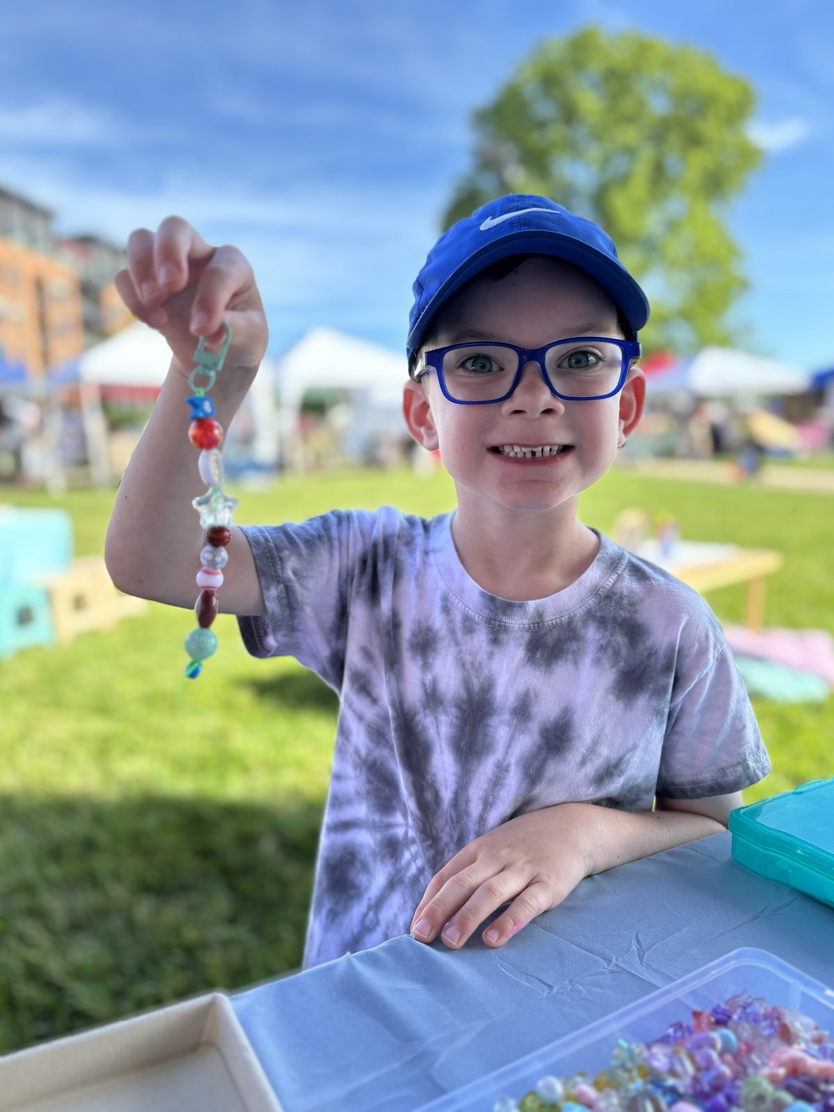 A young guest holding up a beaded creation at a PlayLab Co. station
